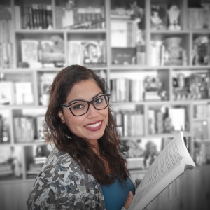 Foto da Mariana Canhoto em frente a uma estante de livros